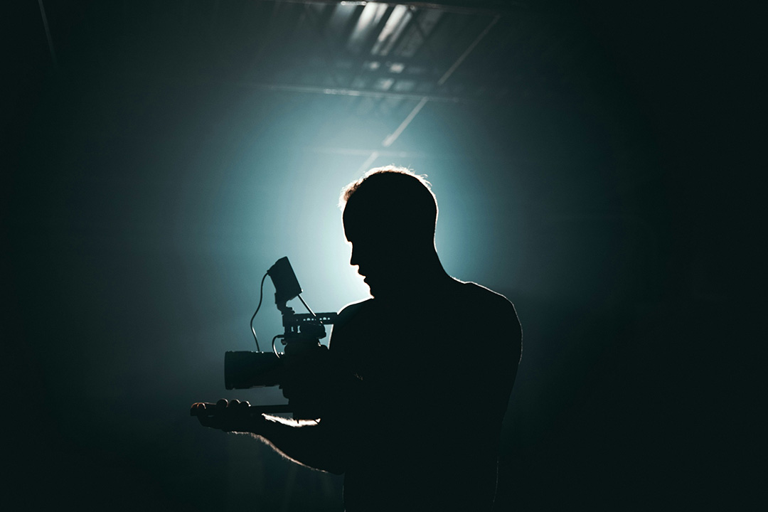 Silhouetted videographer behind the camera in a dark studio, capturing the evolving landscape of modern film production.