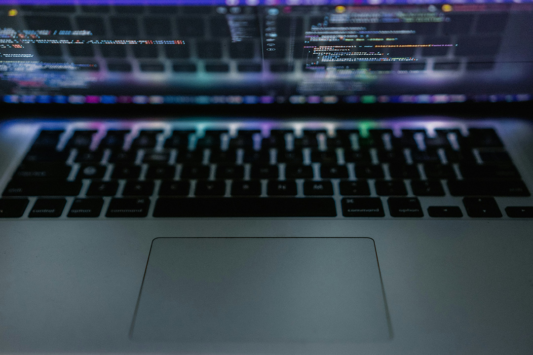 An image of an open laptop with code on the screen and light reflecting to the keyboard representing automation and data-driven ad campaign insights.