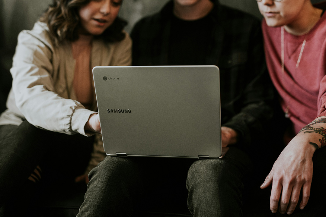 A team of 3 sits together reviewing data from AB testing on a laptop.