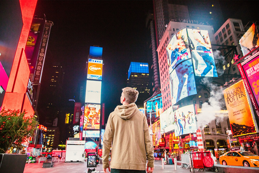 Person standing in Times Square surrounded by digital billboards, symbolizing the impact of marketing in a crowded media landscape.
