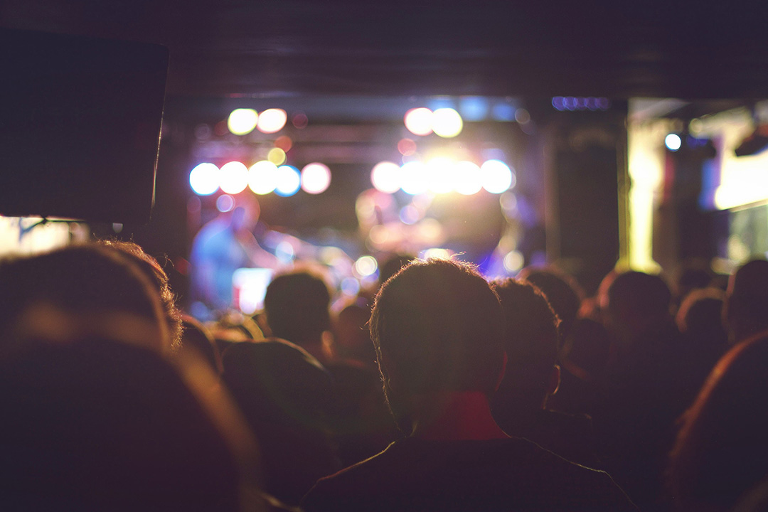 Audience in a dimly lit music venue watching a live band perform under colorful stage lights.