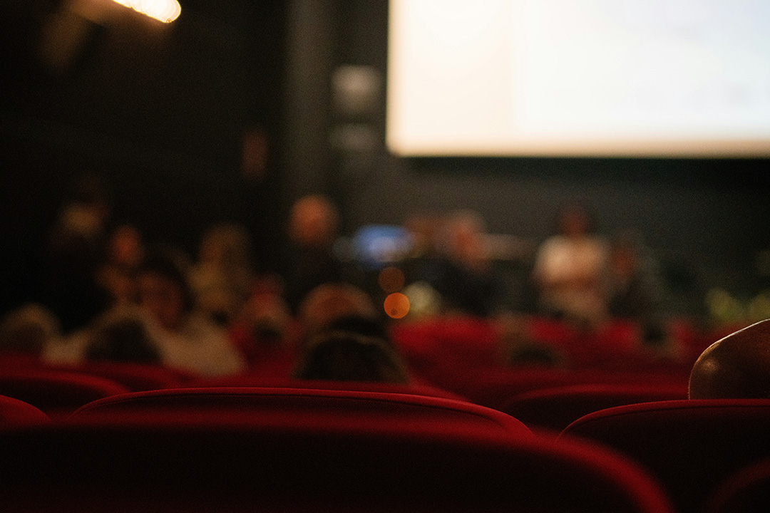 A blurred image of the inside of a movie theater, people sitting in cinema seats waiting for the movie to begin.