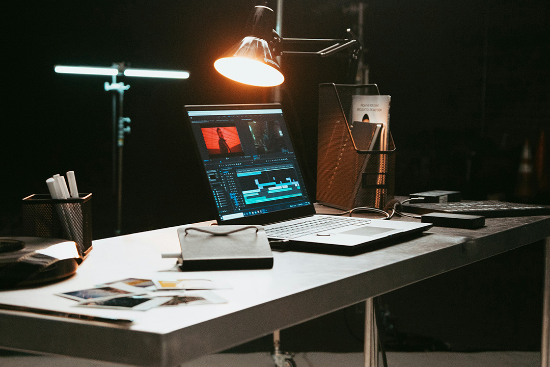 An image of a laptop sitting with a media kit sitting on a desk amongst tools for reviewing photos and text assets