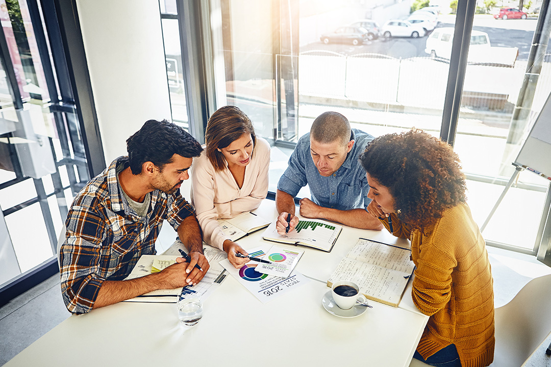 A team of marketers and graphic designers collaborate over analytics and graphics from multivariate testing.
