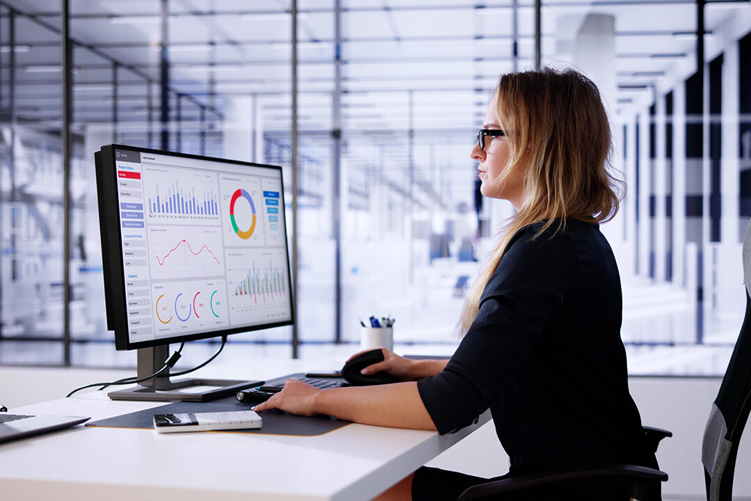 A focused businesswoman in a modern office analyzing marketing analytics on a large screen, featuring graphs, pie charts, and engagement metrics. The image highlights the role of data-driven insights in improving ad targeting, enhancing customer experience, and reducing churn through better marketing strategies.