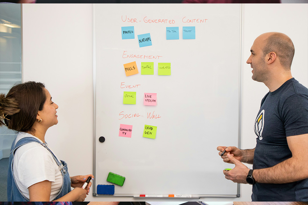 Two creative marketers map out the customer journey with colorful sticky notes in chart fashion along a wall. 